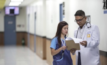 Image with a male and female doctor discussing a patients report in a hospitals corridor